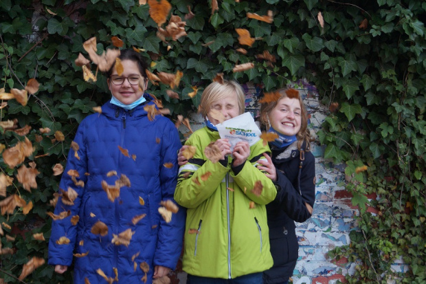drei Mädchen vor einer begrünten Mauer, im Vordergrund fallen braune Herbstblätter