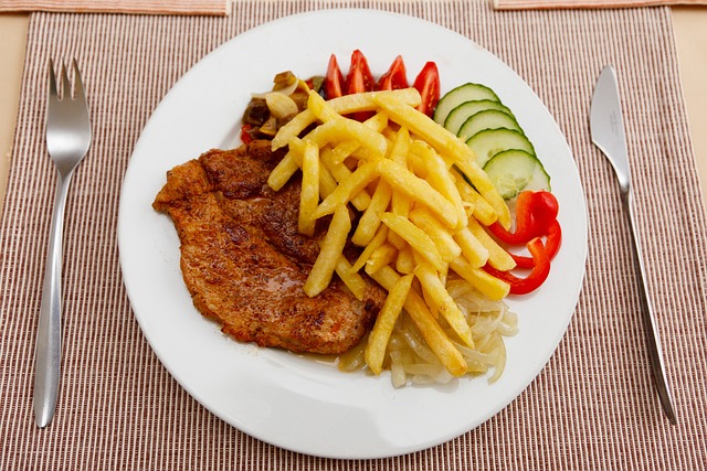 Teller mit Schnitzel, Pommes frites und Gemüse, rechts und links Messer und Gabel
