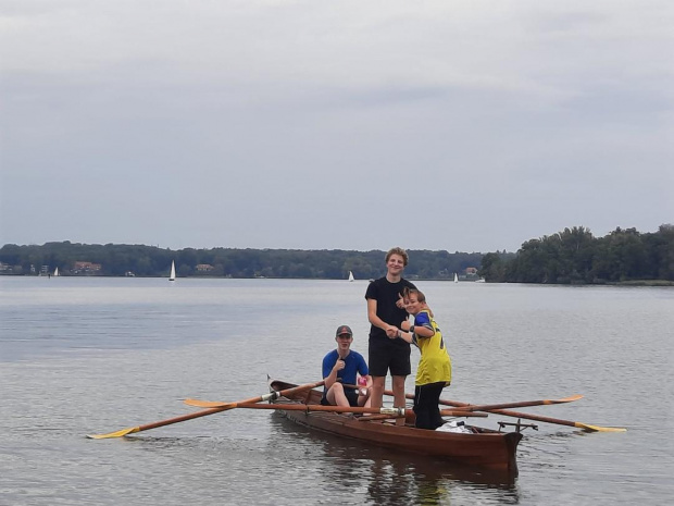 Ruderboot mit drei Jugendlichen (zwei davon stehen) auf einem See