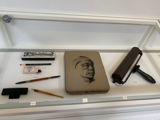 Lithografie-Werkzeuge in einer Ausstellungsvitrine: Stifte, Druckstock, Rolle